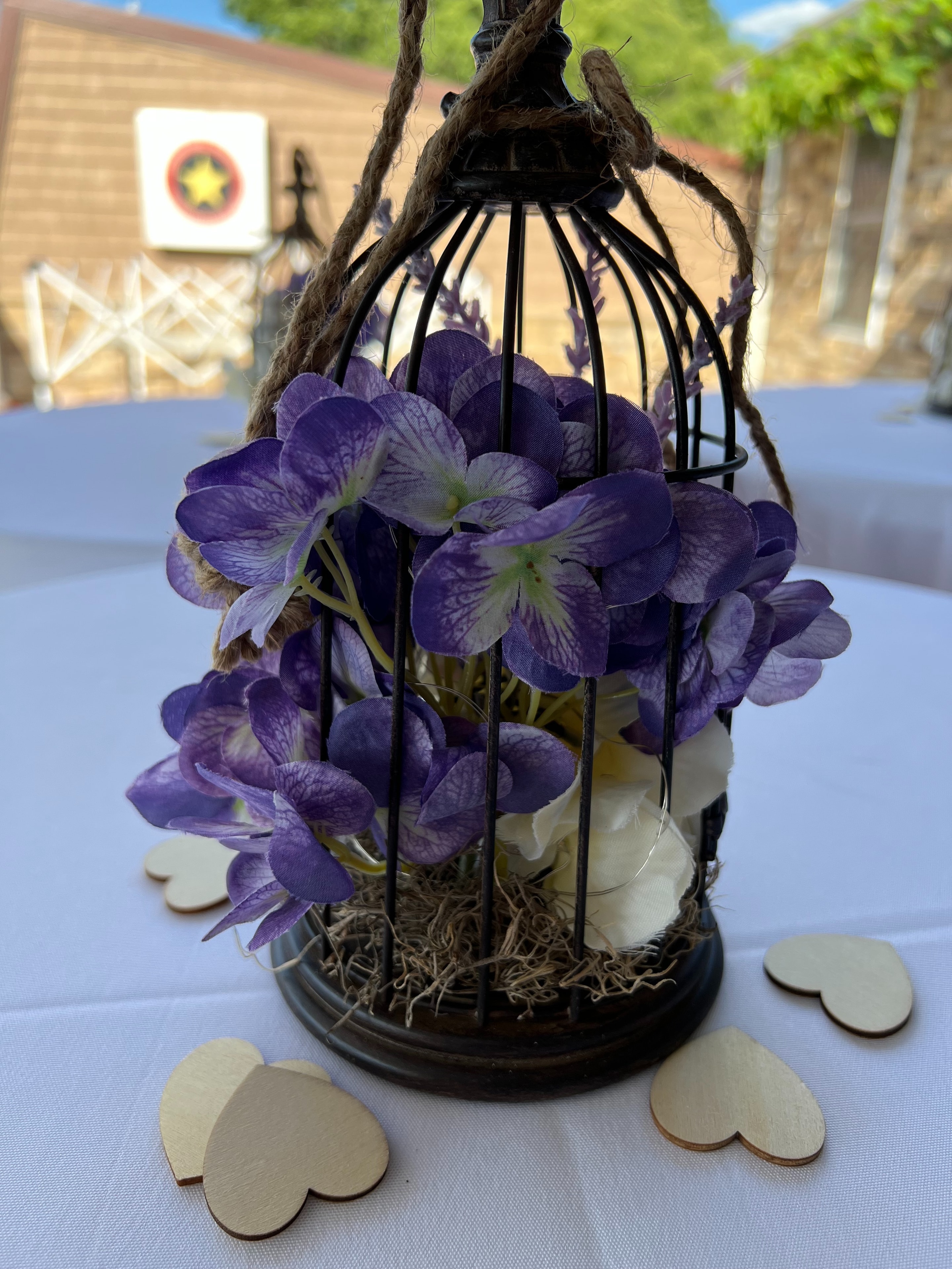 Purple hydrangea birdcage centerpiece with wooden heart confetti on reception table
